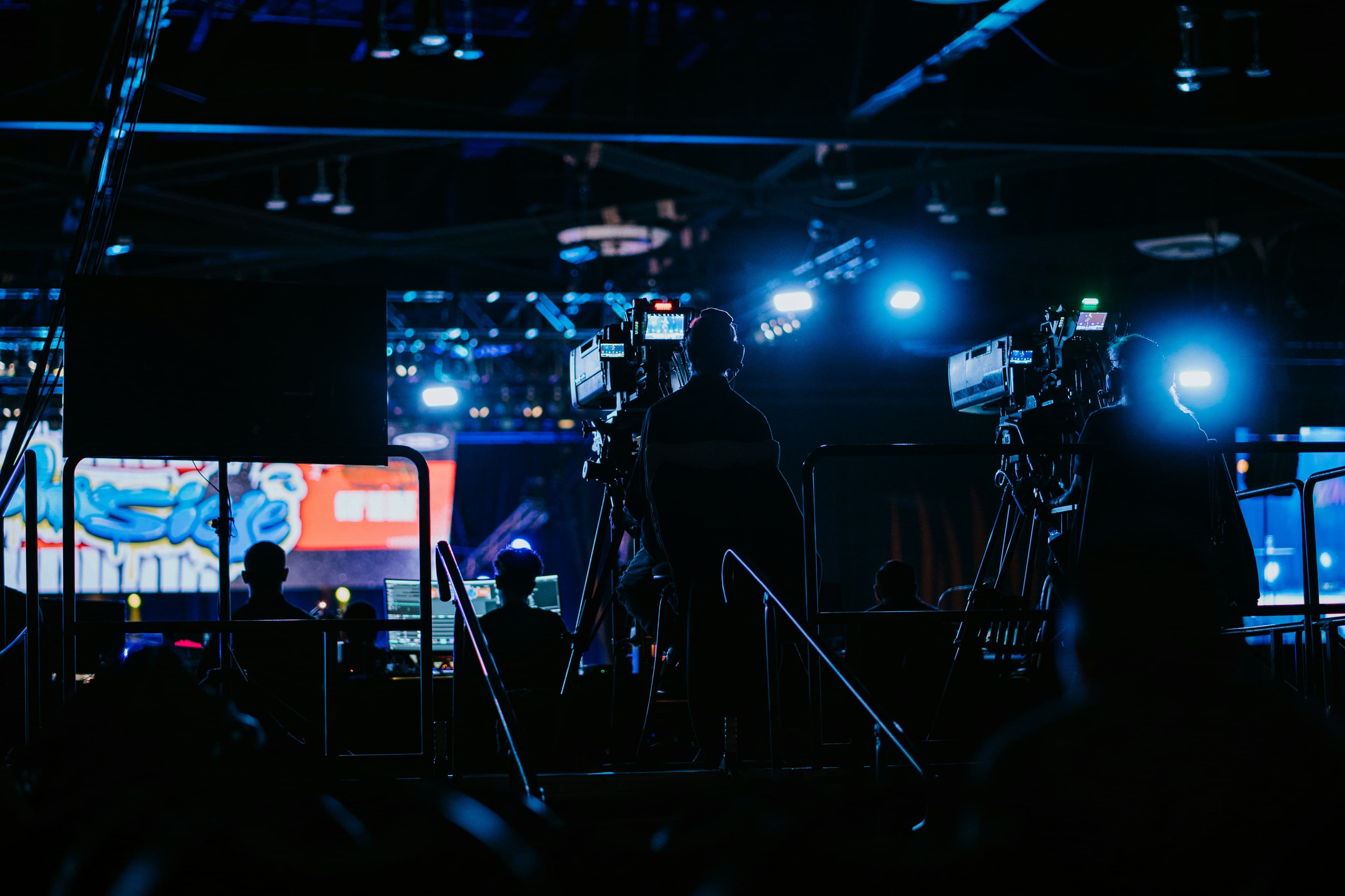 Silhouetted broadcast camera operators film a live event under dramatic blue stage lighting.