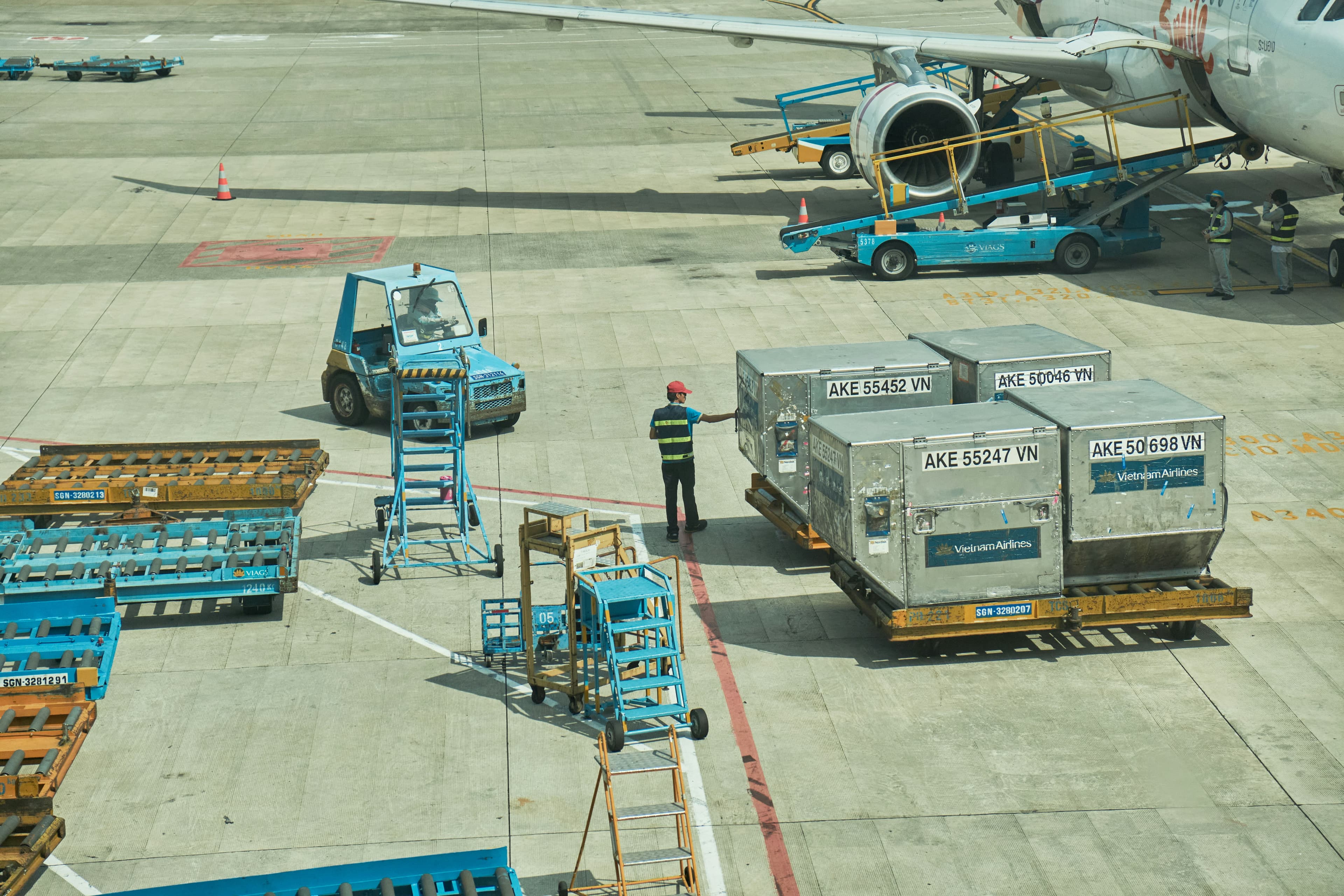 Ground crew worker stands near Vietnam Airlines cargo containers on an airport tarmac.