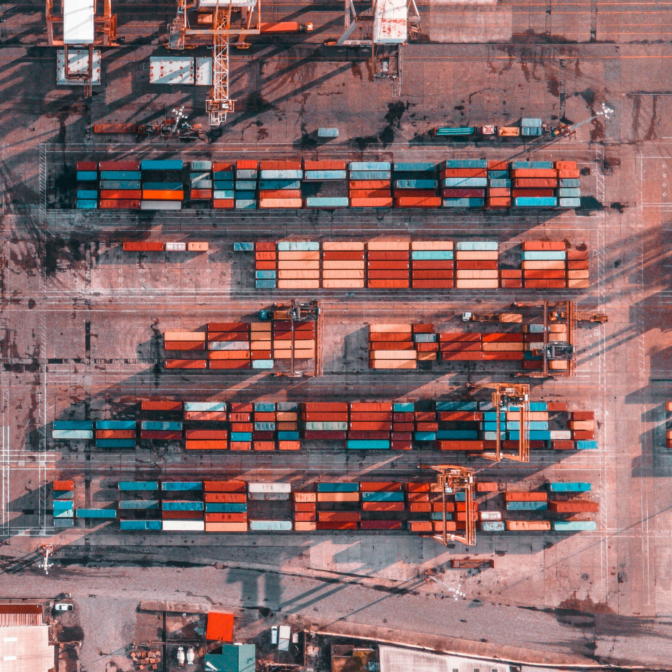 Top-down view of colorful shipping containers stacked in rows at a busy industrial port.