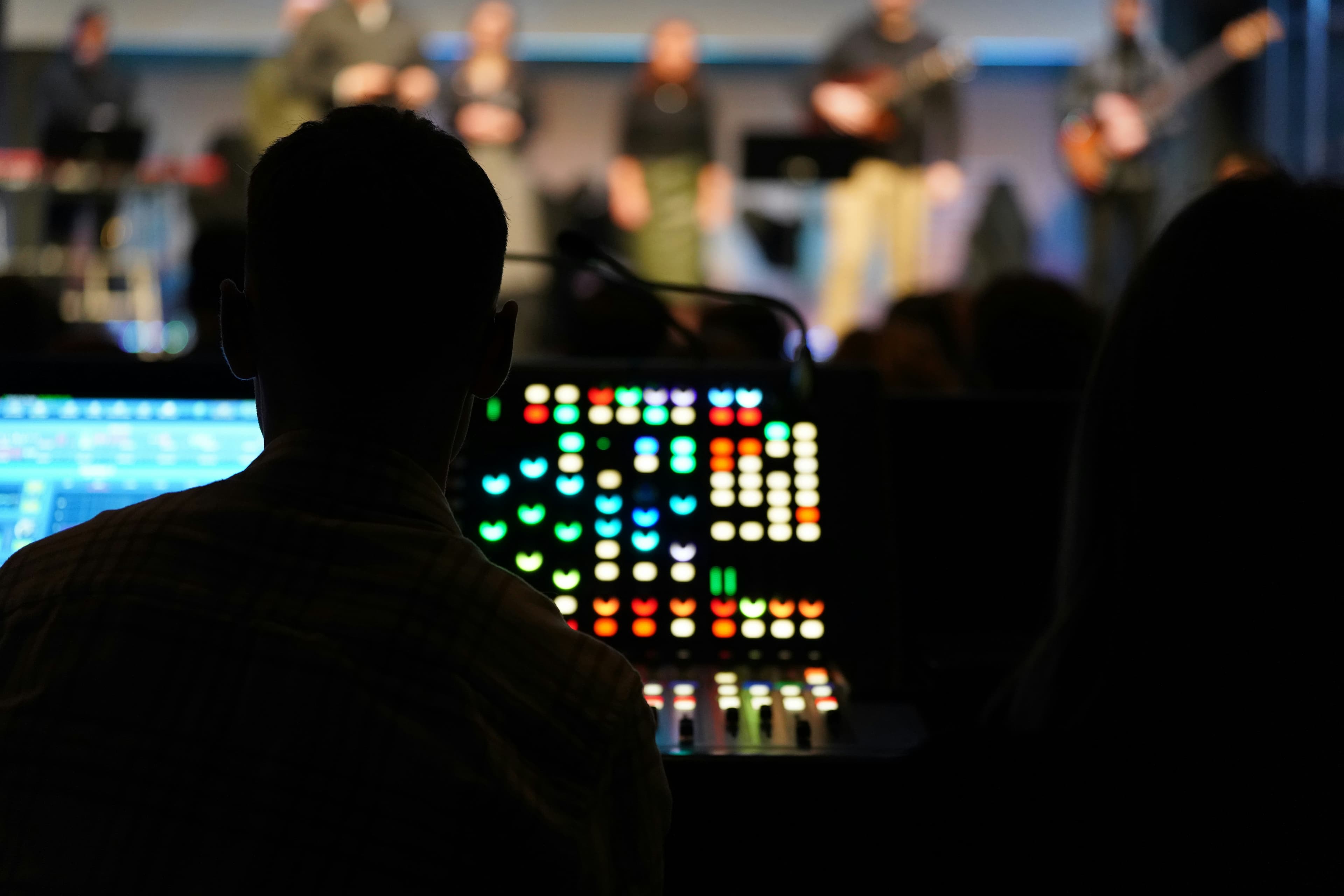 Silhouette of a sound engineer operating a glowing console during a blurred stage performance.